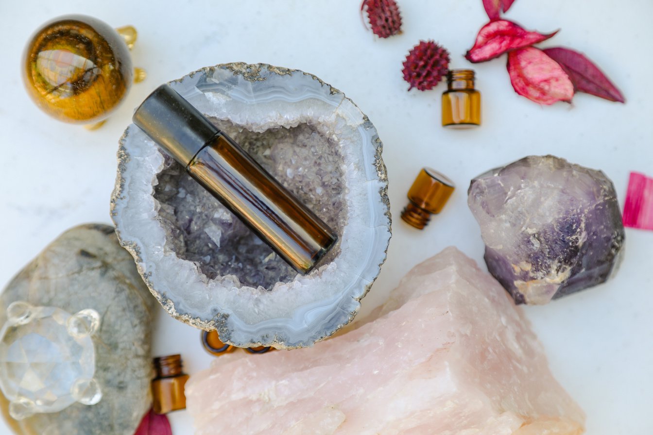 Flat Lay Image Featuring Amber Essential Oils Roller and Sample Drams with Amethyst Geode, Quartz and Crystals